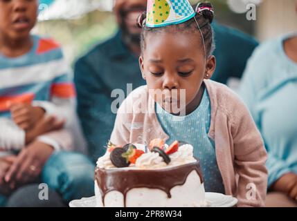 Je fais mon souhait. Une adorable petite fille qui soufflait de bougies pendant sa fête d'anniversaire. Banque D'Images