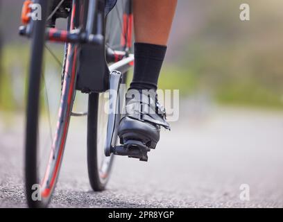 Gros plan des pieds d'une jeune femme qui s'exerce à l'extérieur dans la forêt. Athlète féminine en bonne santé et sportive avec ses pieds sur les pédales pour un cycle. Endurance et cardio pendant une séance d'entraînement dans les bois Banque D'Images