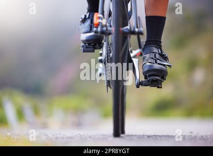 Gros plan d'une femme qui fait du vélo à l'extérieur. Athlète féminine sportive avec ses pieds sur les pédales de vélo tout en faisant un vélo sur une route pour l'exercice. Endurance et cardio pendant une séance d'entraînement et d'entraînement Banque D'Images