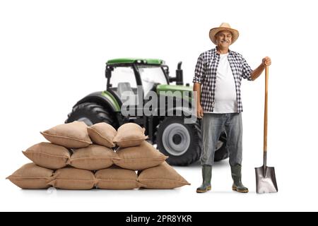 Agriculteur mature avec une pelle et un tracteur vert isolé sur fond blanc Banque D'Images