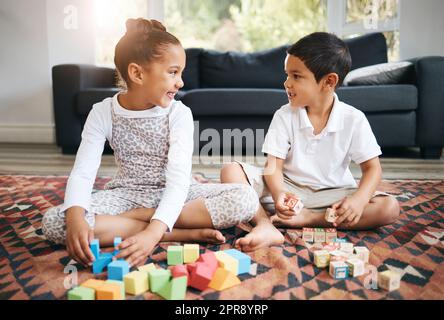 Petits enfants assis sur le sol avec des jouets et des coloriages dans un livre. Petit frère de race mixte et sœur jouant ensemble à la maison Banque D'Images