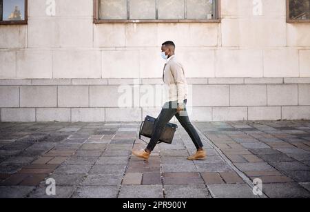 Homme d'affaires noir voyageant seul.Un homme d'affaires afro-américain marchant dans la ville avec ses bagages tout en portant un masque pour se protéger du virus corona dans la ville Banque D'Images