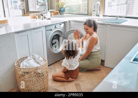 La jeune mère hispanique et sa fille se donnant un haut cinq après avoir fait la lessive à la maison. Adorable petite fille aidant sa mère avec des tâches ménagères Banque D'Images