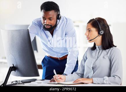 Jeune agent de télémarketing de centre d'appels afro-américain formation d'un nouvel assistant caucasien sur un ordinateur dans un bureau. Solution de dépannage pour chef d'équipe avec stagiaire pour le service client et le support commercial. Des collègues qui utilisent le service d'assistance ensemble Banque D'Images