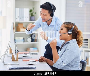 Deux jeunes heureux divers agents de télémarketing de centre d'appels applaudissent avec joie et pointait l'air avec des poings tout en travaillant dans un bureau. Des assistants afro-américains et asiatiques enthousiastes célèbrent les ventes réussies et atteignent des objectifs pour gagner Banque D'Images