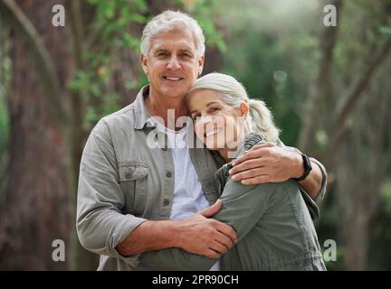 Portrait d'un couple caucasien âgé souriant et regardant heureux dans une forêt pendant une randonnée en plein air. Homme et femme montrant de l'affection et se tenant pendant une pause dans la nature Banque D'Images