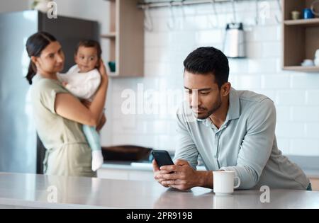 Rappelez-vous toujours ce qui est vraiment important. Un jeune homme ignorant sa femme et son enfant tout en utilisant son téléphone à la maison. Banque D'Images