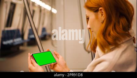 Smartphone Mock Up à écran vert horizontal par une femme regardant un webinaire en ligne sur le transport souterrain. Banque D'Images