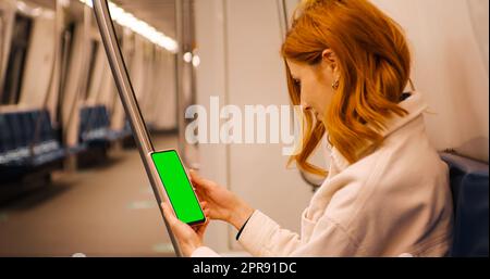 Femme de tourisme assise dans le métro et défile téléphone à écran vert sur le train. Banque D'Images