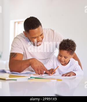 Père de race mixte enseignant le petit fils pendant la classe d'école à domicile. Mignon petit garçon hispanique apprendre à lire et à écrire tandis que son père l'aide. Homme pointant et parlant tout en tutorat d'un enfant Banque D'Images