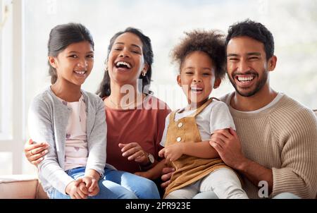 Portrait de famille de race mixte souriante en train de rire et de se détendre sur le canapé à la maison. Parents hispaniques épris sans souci, en lien avec de jolies petites filles. Les enfants heureux passent du temps de qualité avec maman et papa Banque D'Images