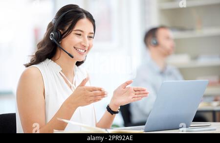 Heres ce que j'avais à l'esprit. Une jeune femme d'affaires portant un casque tout en ayant un appel vidéo sur un ordinateur portable dans un bureau. Banque D'Images