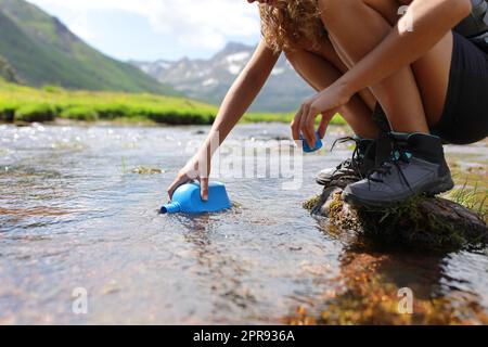Randonneur à la main remplissant la cantine d'eau brute dans une rivière Banque D'Images