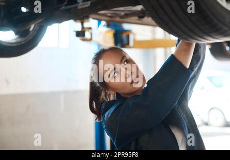 C'est ce que je fais pour détecter des problèmes et faire des réparations. Une femme mécanicien travaillant sous une voiture soulevée. Banque D'Images