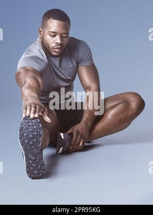 Personne n'aime les muscles durs. Prise de vue en longueur d'un beau jeune homme assis et s'étirant dans le studio. Banque D'Images