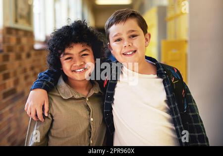 Les amis sont la meilleure partie de l'école. Deux jeunes garçons se tenant dans le couloir de l'école avec leurs bras l'un autour de l'autre. Banque D'Images