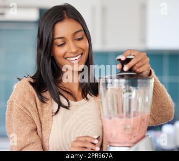 Les smoothies sont chargés de toutes les bonnes choses. Une jeune femme prépare un smoothie sain à la maison. Banque D'Images