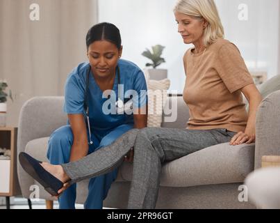 La douleur est-elle pire lorsque vous fléchissez la cheville. Un médecin examine une cheville de femme âgée sur le canapé à la maison. Banque D'Images