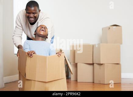Papa sait me faire rire. Un jeune père heureux qui se joint à sa fille et la poussant dans une boîte dans leur nouvelle maison. Banque D'Images