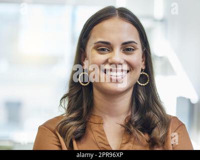 Souriant à la pensée de son propre succès. Portrait court d'une jeune femme d'affaires attirante debout dans son bureau. Banque D'Images