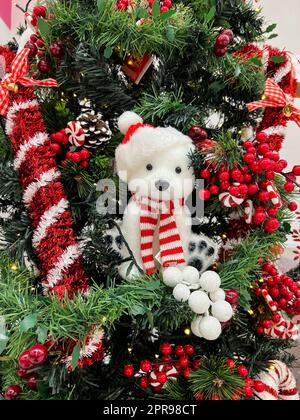 Un petit ours en peluche est installé sur un arbre de Noël décoré de guirlandes, de balles et de bonbons Banque D'Images