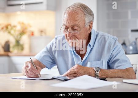 Il semble qu'il soit écrit, mais on ne peut pas lire entre les lignes. Un homme âgé remplissant des formes à la table de cuisine à la maison. Banque D'Images