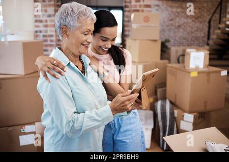 Vos effets personnels pourraient quitter la maison, mais votre cœur ne le fera jamais. une femme âgée regardant une photo avec sa fille tout en emballant des boîtes le jour de déplacement. Banque D'Images