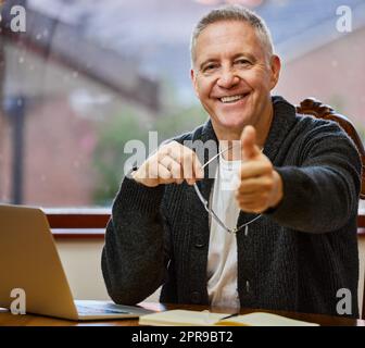 Je suis prêt pour la retraite. Portrait court d'un beau homme âgé qui vous donne les pouces tout en travaillant sur son ordinateur portable dans l'étude. Banque D'Images