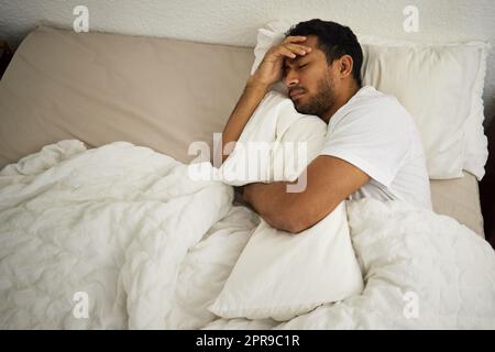 Pendant combien de temps je t'ai à côté. Un homme qui coud un oreiller tout en dormant dans son lit. Banque D'Images