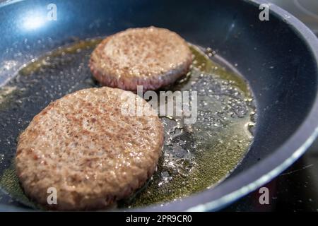 Deux patties hamburger hamburger viande qui se mêle dans une poêle chaude avec de la graisse et de l'huile comme délicieux hamburger barbecue boulettes de viande comme un repas rapide malsain déjeuner avec beaucoup de calories et de cholestérol dans une poêle à frire Banque D'Images