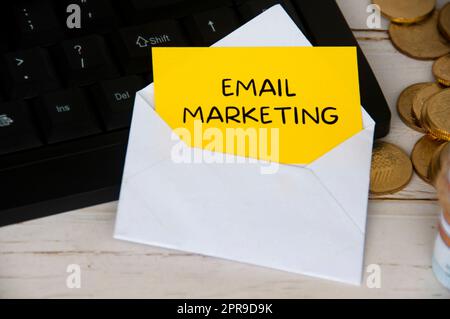 Email marketing texte sur le bloc-notes jaune dans une enveloppe sur ordinateur clavier avec pièces en or. Banque D'Images