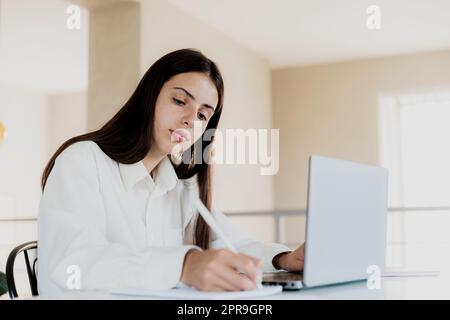 Femme assise au bureau, lisant depuis un ordinateur portable, écrivant des notes sur son ordinateur portable Banque D'Images