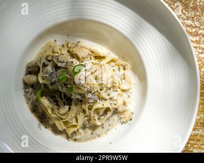 Tagliatelle pâtes avec sauce crémeuse aux truffes blanches au beurre. Pâtes aux champignons termites sauvages surmontées d'une tranche de truffe et d'une cresson. Gros plan cuisine italienne servie sur une assiette ronde profonde. Vue de dessus Banque D'Images