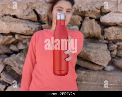 Adolescente à cheveux courts à capuchon rose restant près d'un mur de pierre avec une bouteille d'eau rouge Banque D'Images