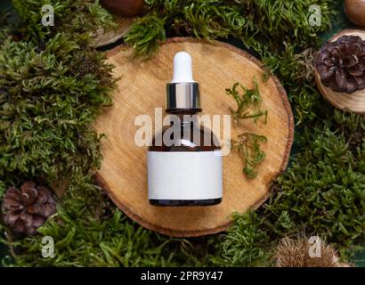 Flacon compte-gouttes en verre brun sur pièce en bois entre mousse verte, vue de dessus, maquette cosmétique naturelle Banque D'Images