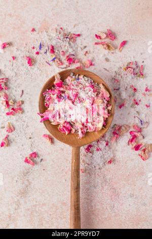 Admirez le sel et les pétales de fleurs séchés dans une cuillère en bois sur une table en marbre rose Banque D'Images