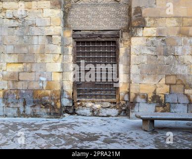 Fenêtre en bois avec grille en fer décorée sur un mur en briques de pierre et un banc de jardin en marbre Banque D'Images