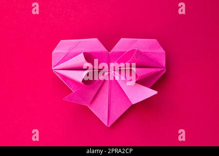 Coeur de papier rose origami isolé sur fond rouge Banque D'Images