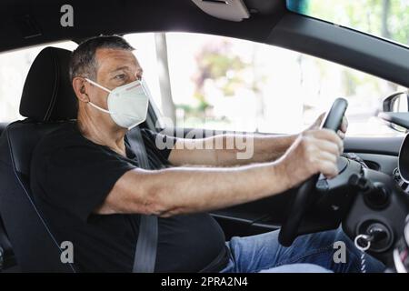 Senior dans sa voiture de conduite de 70s portant un masque facial Banque D'Images