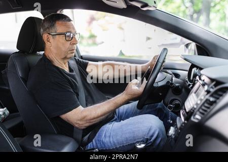 Senior dans sa 70s conduite d'une voiture et à l'aide de son téléphone mobile Banque D'Images