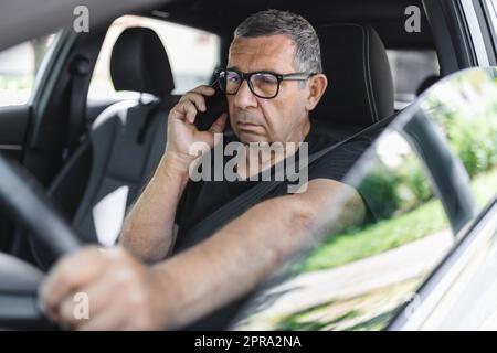 Senior dans sa 70s conduite d'une voiture et à l'aide de son téléphone mobile Banque D'Images