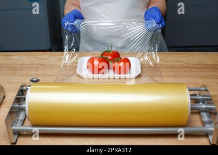 Un employé inconnu s'encapsule dans des tomates en film transparent sur un plateau en plastique blanc Banque D'Images