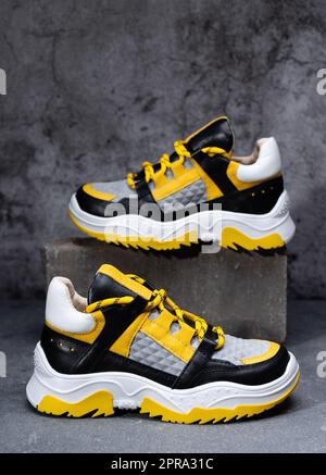 Paire de sneakers brillantes élégantes en jaune, noir et blanc sur fond de béton gris. Banque D'Images