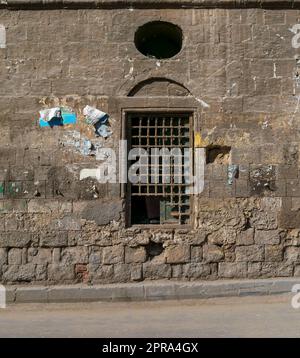 Vieux mur de briques de pierre abandonnée avec une fenêtre en bois cassée de grunge fermée recouverte de grille en bois Banque D'Images