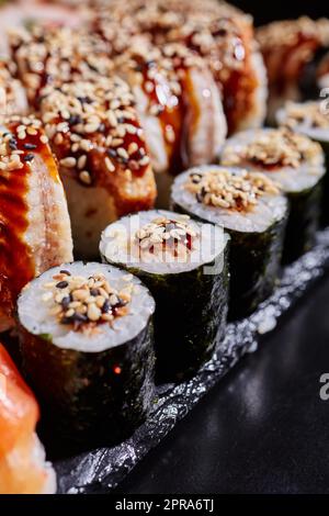 Gros plan de sushi maki avec thon, sauce et graines de sésame sur le bord d'une assiette en pierre noire. Banque D'Images