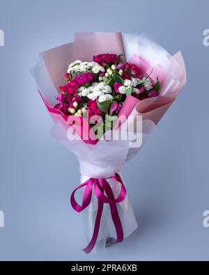 Bouquet de fleurs roses et blanches enveloppées de papier floral sur fond bleu. Banque D'Images