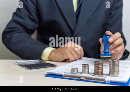 Homme d'affaires tenant un tampon en caoutchouc pompant des documents d'approbation financière ou de prêt bancaire sur le bureau.Business concept d'investissement. Banque D'Images