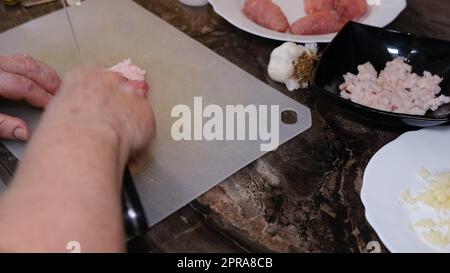 Une vieille femme hache du porc cru sur une planche à découper avec un couteau Banque D'Images