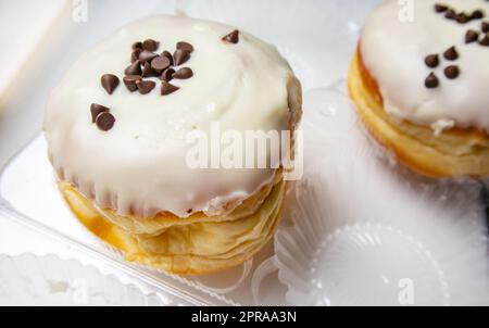 Deux délicieux beignets avec sucre glace et copeaux de chocolat sur fond blanc dans un récipient en plastique transparent Banque D'Images