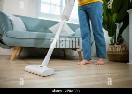 Bonne jeune femme asiatique avec aspirateur à accumulateur à la maison dans le salon Banque D'Images